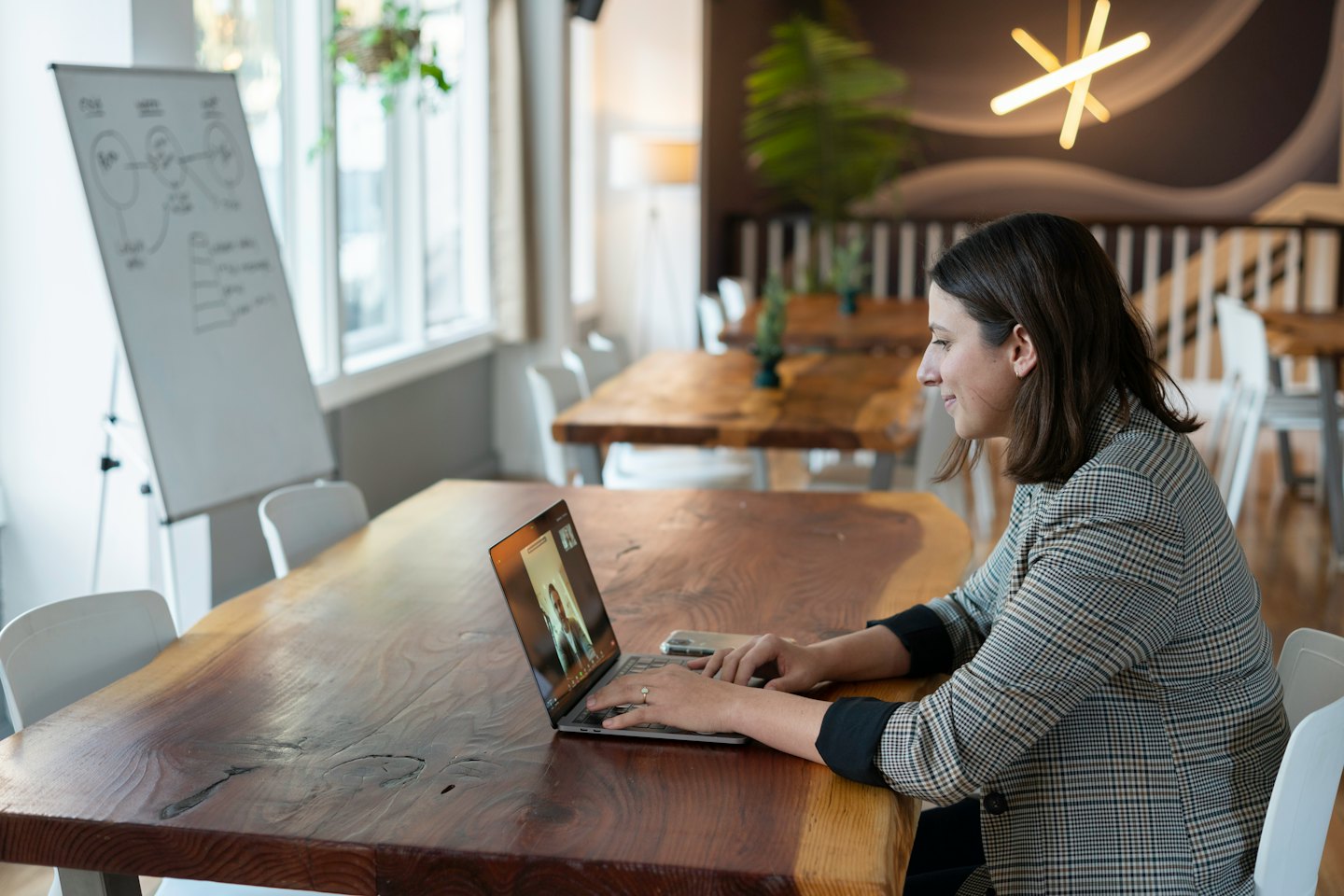 Woman on video call at a large live-edge wooden table.